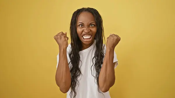 stock image Angry young african american woman clenching fists against a yellow isolated background