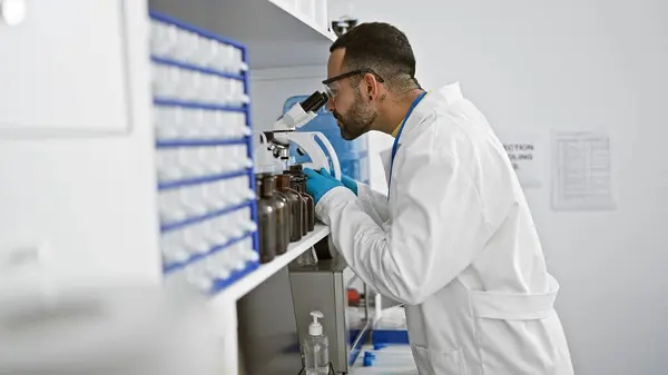 stock image Hispanic man with beard working in laboratory analyzing samples through microscope