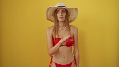 Yaz bikinili bir kadın, şapkasıyla gizli bir beyaz kadını fısıldıyor sarı arka planda dedikodu yapıyor, ağzı el ele konuşmalarla kaplı.