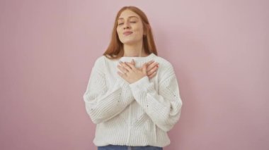 Gülümseyen genç kızıl, minnet duyuyor, ayakta duruyor, elleri göğsünde, pembe bir kazak içinde. bakım, sağlık ve canlı yaşam biçimi tasvir edilmiştir.