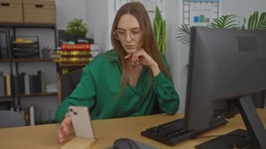 Ofis odasında akıllı telefon ve bilgisayar kullanan bir kadın. Arkaplanda bitkiler ve kitaplar var.