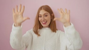 Neşeli genç kızıl saçlı kadın parmaklarıyla on numarayı gösteriyor, pembe bir arka plana karşı duruyor, mutlu bir şekilde yukarı bakıyor..