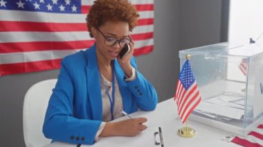 Mavili Afrikalı Amerikalı kadın oy sandığının yanında akıllı telefonuyla çalışıyor. Seçim merkezinde bizimle birlikte..