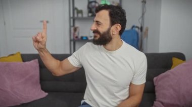Beyaz tişört giyen orta yaşlı İspanyol bir numarayı gösterip işaret ederken kendinden emin ve mutlu gülümsüyor. evde.