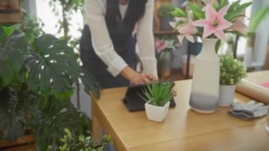Çiçekçi dükkanında tablet kullanan olgun İspanyol kadın. Etrafı bitki ve dekorasyonlarla çevrili..