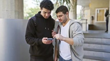 Şehir basamaklarında akıllı telefon kullanan iki adam, şehir ortamında dostluk ve teknoloji kullanımı yapıyorlar..