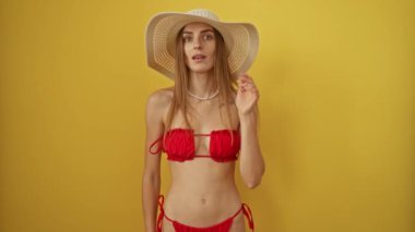 Bikinili bir kadın, yaz şapkalı, dedikodu ve söylentilere kulak misafiri, sarı arka planda izole edilmiş - Kafkas güzelliği yazı ve sırları kucaklıyor