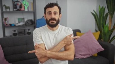 Beyaz tişörtlü kafası karışmış orta yaşlı bir adam, vurgulu bir şekilde farklı yönleri işaret ediyor, evdeki anlaşmazlığı dile getiriyor.