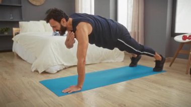 Aktif kıyafetli formalı bir adam modern bir yatak odasındaki yoga minderinde şınav çeker..