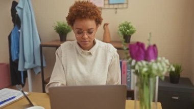 Neşeli Afro-Amerikalı kadın evinde oturuyor, masada el hareketleriyle mutlu bir şey sunuyor, gülümsüyor ve işaret ediyor, kameraya bakıyor..