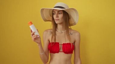 Bikinili kadın elinde güneş kremi, kendine güvenen, kendine güvenen, ayık, sarı arka planda izole bir kadın.