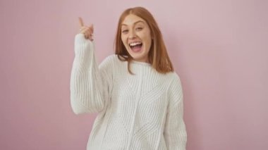 Zeki, genç, kızıl saçlı bir kadın, mutluluk saçıyor, süveter giyiyor ve pembe arka planda dikiliyor, başarılı bir fikri işaret eden 