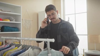 Parlak, iyi organize edilmiş bir soyunma odasında kıyafetlere bakarken akıllı telefondan konuşan şık bir genç adam..