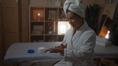 Kaplıca sağlık merkezinde beyaz bir bornoz ve havluyla birlikte mum ışığında bir güzellik odasına krem süren esmer bir kadın..