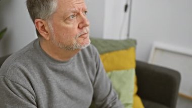 Olgun, gri saçlı bir adam. Kapalı bir koltukta otururken göğsünde ağrı hissediyor. Rahatsızlık belirtileri gösteriyor..