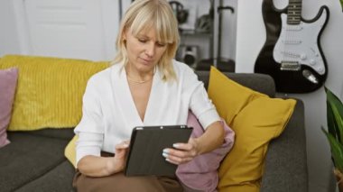 Blonde woman using tablet on couch in modern living room