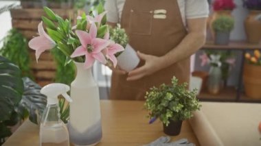 Gözlüklü ve önlüklü yaşlı bir adam güneşli bir çiçekçide saksı bitkisinin kokusundan hoşlanır.