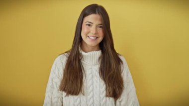 Gülümseyen genç İspanyol kadın, başarı fışkırıyor, sarı izole arkaplanda süveter içinde geriye doğru parlıyor.