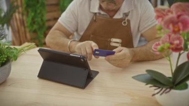 Çiçekçide tablet kullanan kredi kartı olan olgun bir adam.
