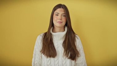 Süveter giyen genç, güzel bir İspanyol kadın. Parmak parmağa, burun buruna, neşeyle gülümsüyor. İzole edilmiş sarı arkaplan üzerindeki güzellik kavramı