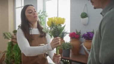 Önlüklü kadın çiçekçi, sarı laleleri hoş çiçekçi dükkanındaki adama sunuyor.