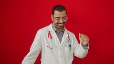 Doktor üniformalı genç İspanyol, başarıyı heyecanlı bir jestle kutluyor ve izole edilmiş kırmızı arka planda çığlık atıyor.