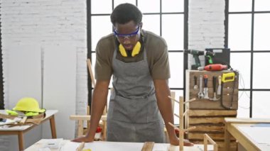 Ahşap ve aletlerle dolu bir atölyede kolları kavuşturulmuş kendinden emin genç zenci marangoz..