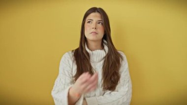 Düşünceli bir ifadeyle düşünceli genç İspanyol bir kadın, parmakları çenesinde, düşüncelerinde kaybolmuş, tek başına duruyor, şüphe içinde, parlak sarı bir arka plan üzerine bir süveter giyiyor..