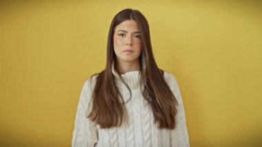 Öfkeli genç İspanyol kadın şiddeti tehdit ediyor, izole edilmiş sarı arka plandaki bir bıçak gibi boğazını kesiyor. Hırka giyiyor, öfkeli bir tasvirde saldırganlık gösteriyor.