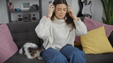 İspanyol kadın kulaklıkla müzik dinliyor, rahat oturma odasında bisiklet teriyeriyle rahatlıyor..