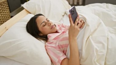 Genç bir İspanyol kadın, yatak odasında akıllı telefonunda bir mesaj okurken şaşırmış görünüyor..