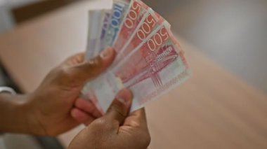 Kapalı mekanda bir adamın İsveç banknotlarını saydığı yakın plan.