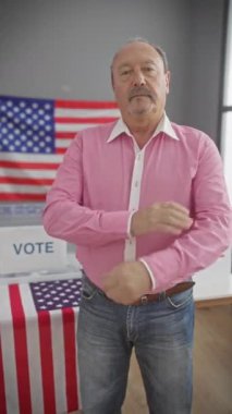 Kollarını kavuşturmuş kendinden emin kıdemli bir adam Amerika 'da seçim içlerinde bayrak ve oy işaretiyle duruyor..