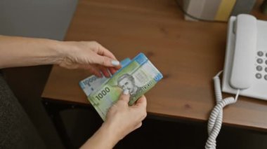 İyi aydınlatılmış bir ofis ortamında telefon başında Şili pezosu sayan eller.