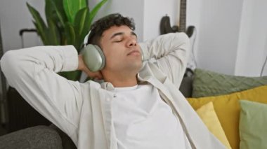 Kulaklıklı rahat bir adam modern bir oturma odasında müziğin tadını çıkarıyor.