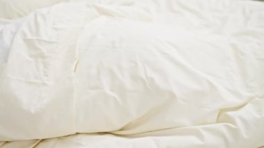 Parlak, rahat bir yatak odasında beyaz çarşaflı bir yatakta huzur içinde uyuyan genç bir adam.