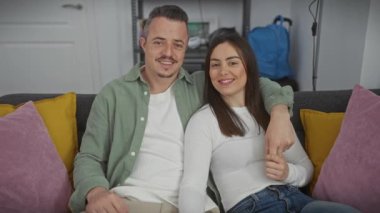 Sevgi dolu bir erkek ve kadın, renkli yastıklarla çevrili, rahat bir evde, bir kanepede birlikte otururlar..