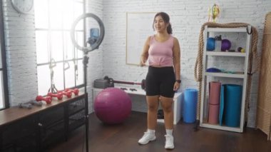 Spor salonunda egzersiz yapan, gülümseyen ve spor yapan, spor aletleriyle çevrili, halterler, egzersiz topları ve kapalı bir spor merkezinde paspaslar olan genç bir kadın..