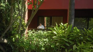 Huzurlu bir kadın, tropik yapraklarla çevrili bereketli bir bali tatil köyünün terasında içki içmekten zevk alır..