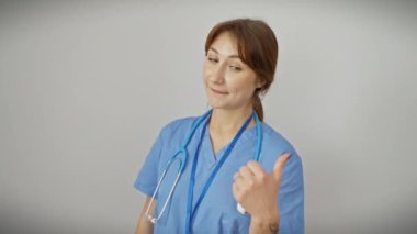 Steteskop takmış, gülümseyen, gülümseyen ve baş parmağıyla yan tarafı gösteren beyaz bir kadın. izole edilmiş beyaz arkaplan