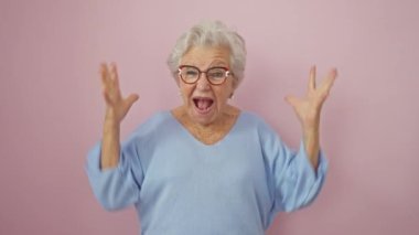 Gözlüklü çılgın, gri saçlı, çılgın bir zaferin kutlamasına yakalanmış, kollarını kaldırmış, canlı, izole pembe arka plandaki başarısından dolayı sevinçten havalara uçmuş..