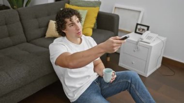 Gündelik kıyafetli genç bir İspanyol, modern bir oturma odasında bir kupayla rahatlar..