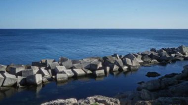 Gelibolu, puglia, İtalya 'nın sahil şeridinde beton bloklar, berrak bir gökyüzünün altında, arka planda mavi deniz ve kayalık kıyılar var..