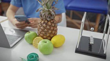 Ananas, yeşil elma, limon ve dizüstü bilgisayarla kliniğin masasında akıllı telefon kullanan bir kadın sağlık ve sağlık konularını çağrıştırıyor..