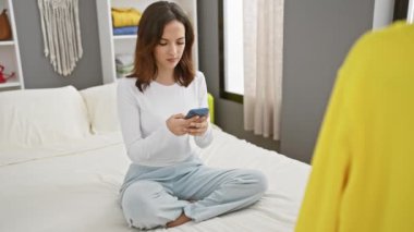 Yatak odasının içinde akıllı telefon kullanan İspanyol kadın.