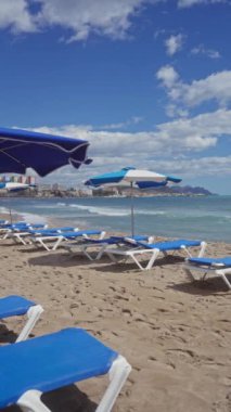 Boş mavi güneş şezlongları ve şemsiyeleri bulutlu bir gökyüzünün altında huzurlu bir sahil manzarası..