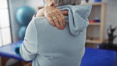 Orta yaşlı bir kadın fizyoterapi kliniğinde sırt ağrısı çekiyor. Eline ve duruşuna odaklanıyor..