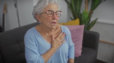 Evde oturan ve göğsünü tutan yaşlı bir kadın muhtemelen kalp sorunu yaşıyor.
