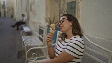 Lecce, İtalya 'da bir kadın, sevimli bir kasaba sokağındaki bankta otururken dondurma külahını yemekten hoşlanır..