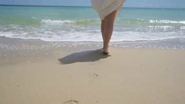 Pescoluse, puglia, salento, İtalya 'da, güneşli bir günde, kumlu sahilde ayaklarına hafif dalgalar değen beyaz elbiseli genç İspanyol kadın..